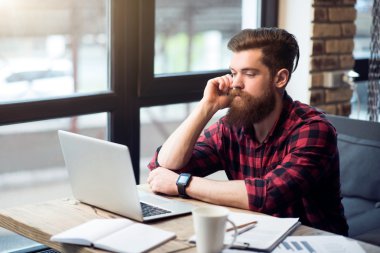 Yakışıklı sakallı adam masada oturuyor.