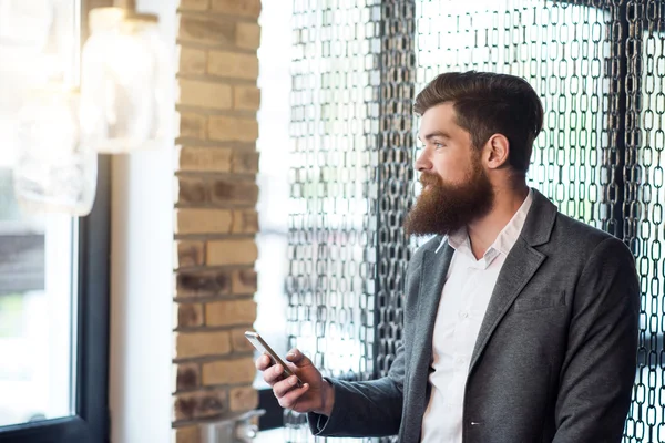 Приятный позитивный бородатый мужчина держит мобильник — стоковое фото