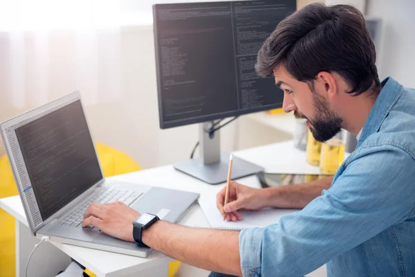 Homem olhando para laptop e tomando notas — Fotografia de Stock