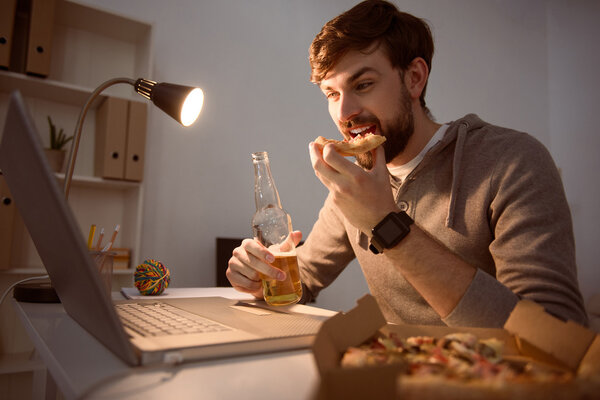 Man eating pizza and looking at computer