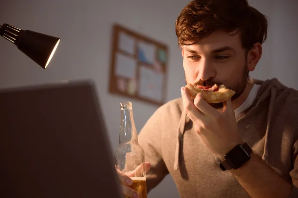 Uomo che guarda lo schermo e mangia pizza — Foto Stock