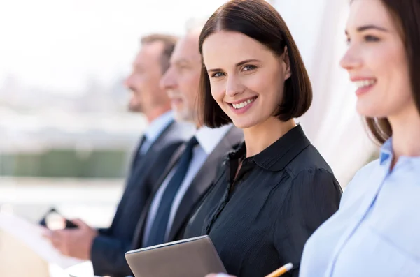 Mujer alegre de pie con sus colegas — Foto de Stock