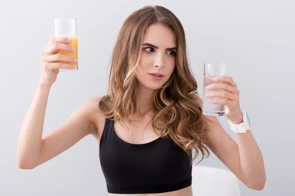 Pleasant puzzled woman holding glasses of water and juice — Stock Photo, Image