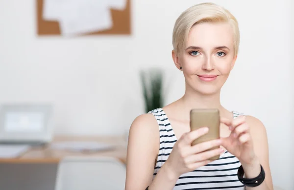 Mulher olhando para a câmera e segurando smartphone — Fotografia de Stock