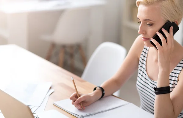 Woman taking notes and talking on smartphone — Stock Photo, Image