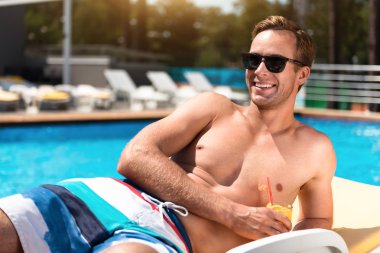 Yüzme havuzu yakınında dinlenen mutlu gülümseyen adam