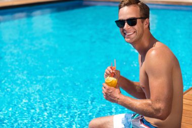 Positive man sitting near swimming pool clipart