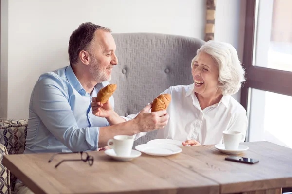 Joyful senior couple eating croissants.