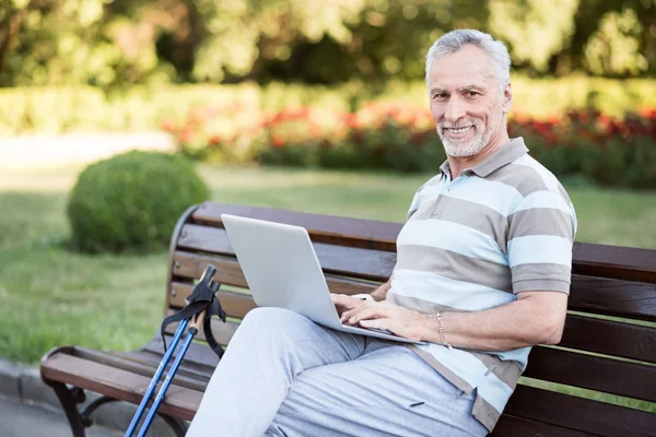 Stylish handsome old man sitting in a park wearing sportswear. — Stock Photo, Image