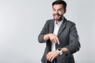 Gülümseyen sakallı adam akıllı saatini işaret ediyor.