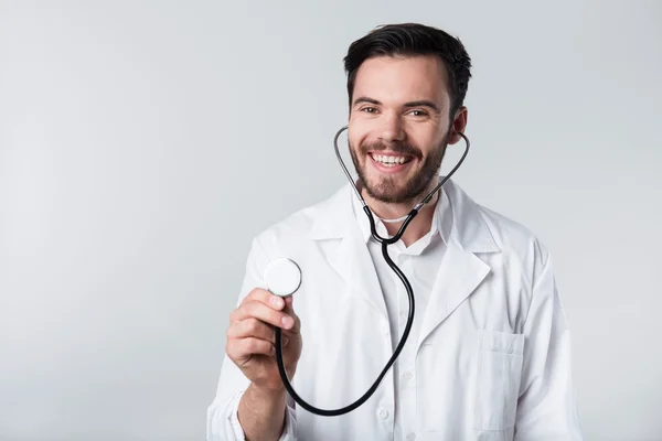 Hombre barbudo contento sonriendo y sosteniendo estetoscopio . — Foto de Stock