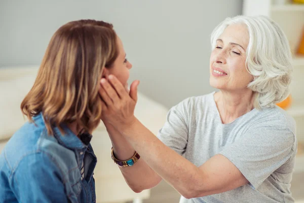 Deliziosa donna anziana amorevole che tiene le guance di sua figlia — Foto Stock