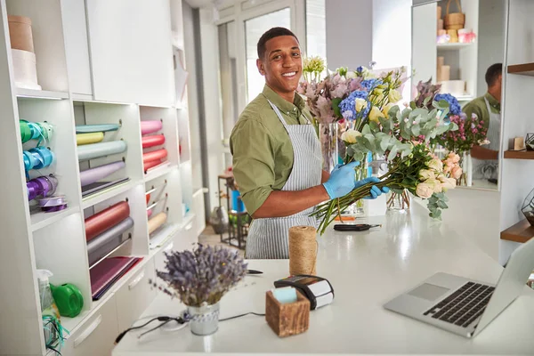 Radosny młody człowiek pracujący z gadżetami w kwiaciarni — Zdjęcie stockowe