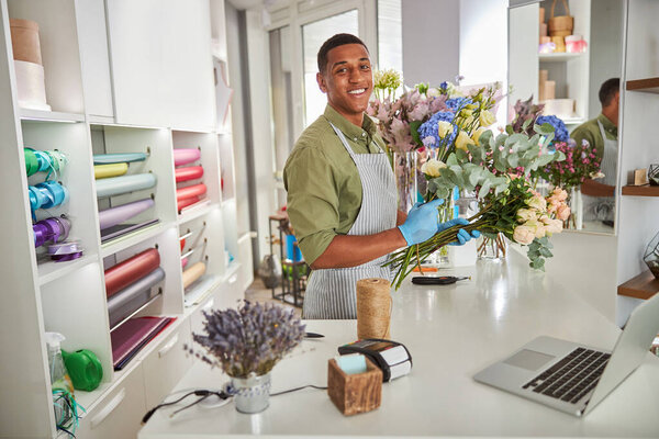 Joyful young man working with gadgets in flower shop