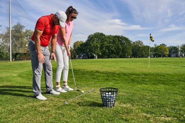 Ciddi bir golf hocası, bir kadın öğrenciye ders veriyor.