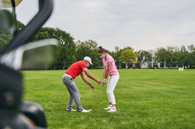Maskeli bir koç müşterisine golf temellerini öğretiyor.