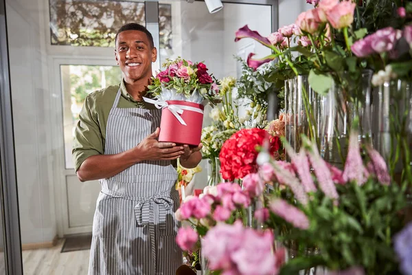 Vänlig florist visar en kruka bredvid blomsterhyllan — Stockfoto