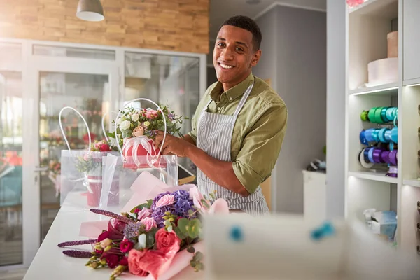 Assistente de loja de flores satisfeito segurando um pote acima de uma bolsa — Fotografia de Stock