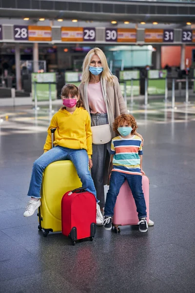 Мати обіймає двох дітей, які сидять на валізах — стокове фото
