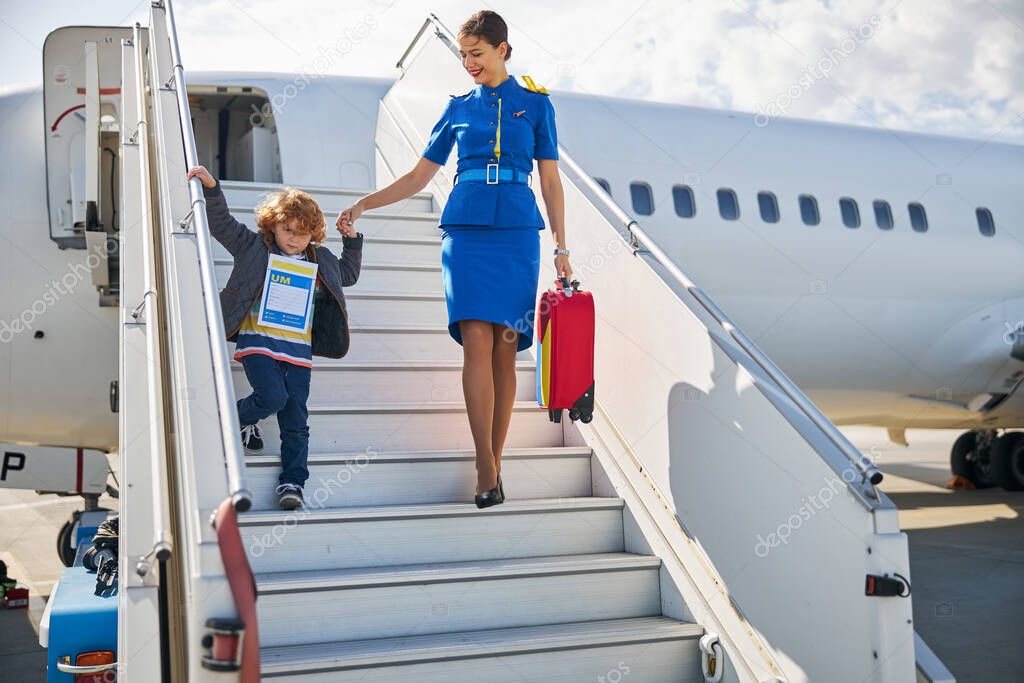 Helpful airline hostess assisting a kid in exiting an aircraft