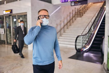 Yüz maskeli bir iş adamı telefon görüşmesi yapıyor.
