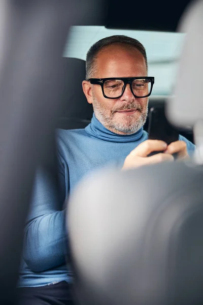 Сосредоточенный мужчина пишет смс на заднем сиденье такси — стоковое фото