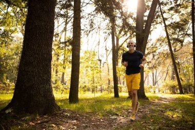 Neşeli kır saçlı erkek güneşli ormanda koşuyor.