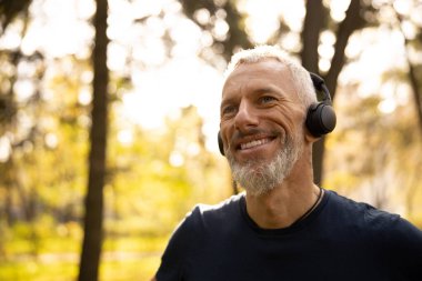 Mutlu sakallı adam doğada müzik dinliyor.