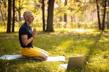 Sakin ol, olgun erkek dışarıda laptopla meditasyon yapıyor.