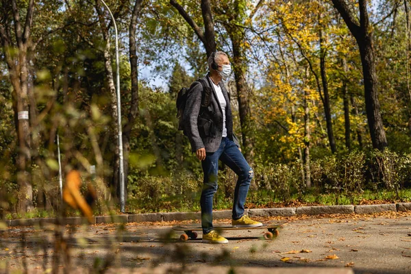 Grizzled fit guy in mask is skateboarding in open air — Stock Photo, Image