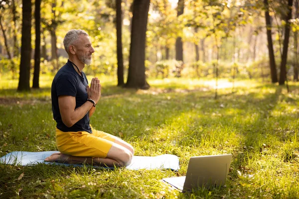 Calma macho maduro haciendo meditación con el ordenador portátil al aire libre —  Fotos de Stock