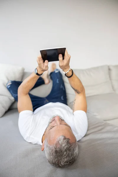 Adulto acostado en un sofá con una tableta — Foto de Stock