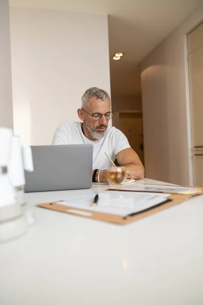 Сосредоточенный мужчина делает заметки перед ноутбуком — стоковое фото