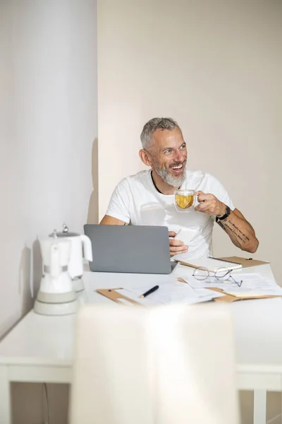 Взрослый наслаждается чаем, работая за ноутбуком — стоковое фото