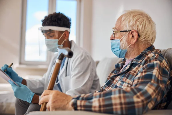 Hombre de edad en una máscara mirando a un médico — Foto de Stock