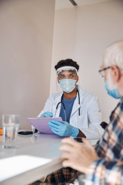 Hasta durumunu inceleyen bir not panosuyla yaşlı bir doktor.