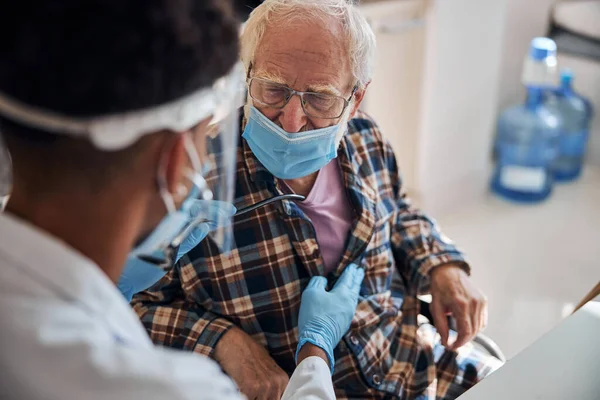 Profesional de la salud auscultando al anciano hombre caucásico — Foto de Stock