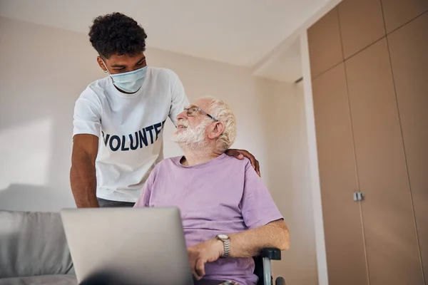 Nöjd manlig pensionär som ler mot en volontär — Stockfoto