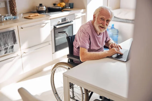 Пенсионер за компьютером на кухне — стоковое фото