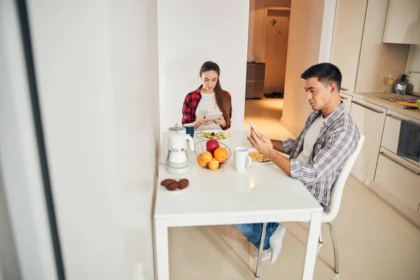 Giovane coppia utilizzando i loro gadget a colazione — Foto Stock