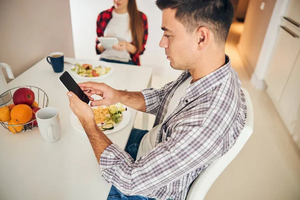 Два молодых супруга используют свои гаджеты за обедом — стоковое фото