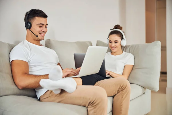 Morena homem e linda senhora sentada no sofá com laptops — Fotografia de Stock