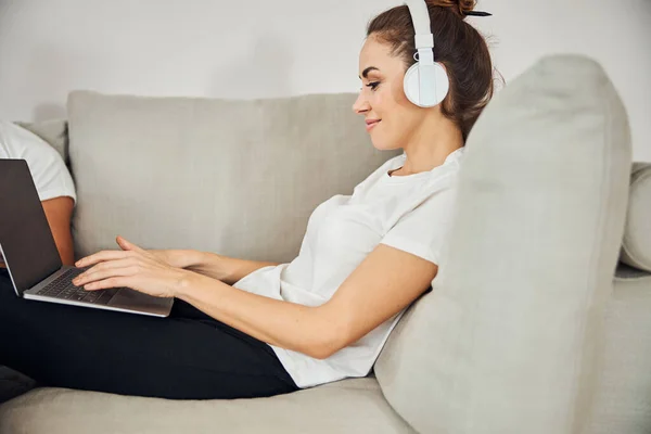 Linda senhora em fones de ouvido trabalhando em seu laptop de casa — Fotografia de Stock