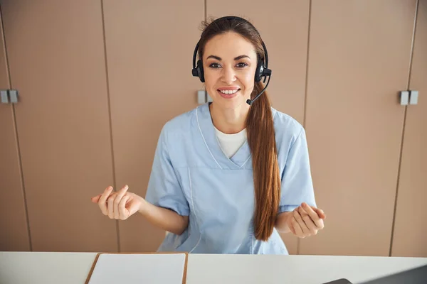 Beautiful female medical worker in headset making hand gestures — Stock Photo, Image