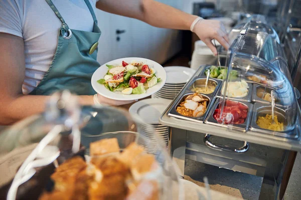 Airport cafe employee adding more food to the plate — Stock Photo, Image