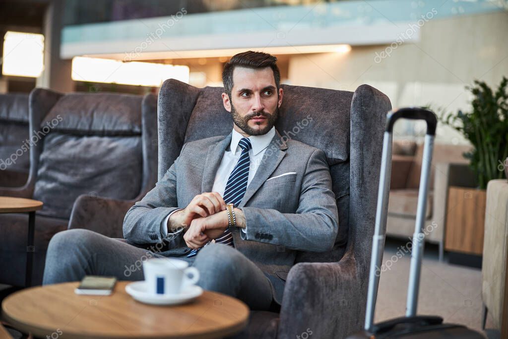 Serious entrepreneur in an armchair setting the watch on his left hand to the right time