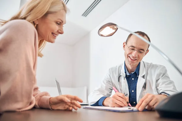 Усміхнений лікар пише в присутності свого пацієнта — стокове фото