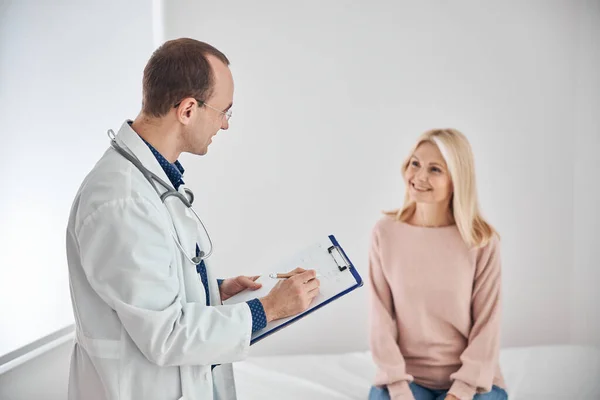 Sorridente medico dai capelli scuri intervistando la bella paziente donna — Foto Stock