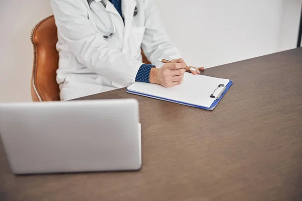 Médico com uma caneta na mão sentado na mesa — Fotografia de Stock