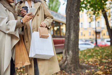 Kahve içen ve sokakta cep telefonu kullanan bayan arkadaşlar.
